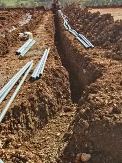 An open trench with lengths of conduit laid along it