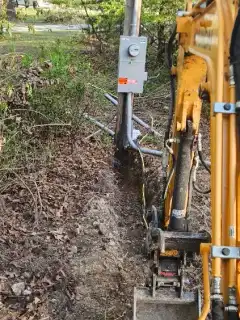 A mini excavator working beside a meter pole and conduit trench