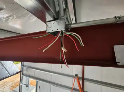 A junction box and wires hanging from a red steel beam
