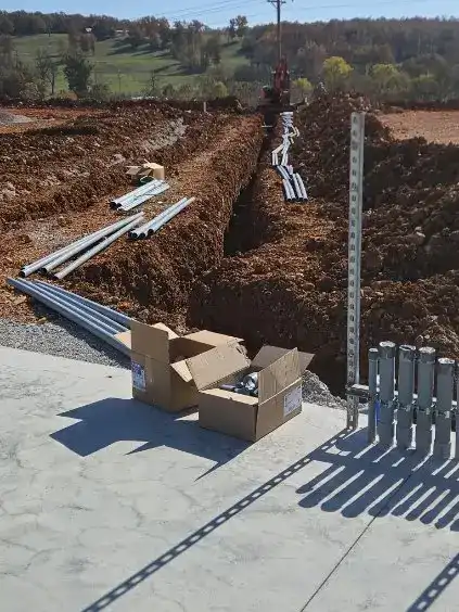 Conduit stub-ups on a strut stand beside an open trench with lengths of conduit laid out