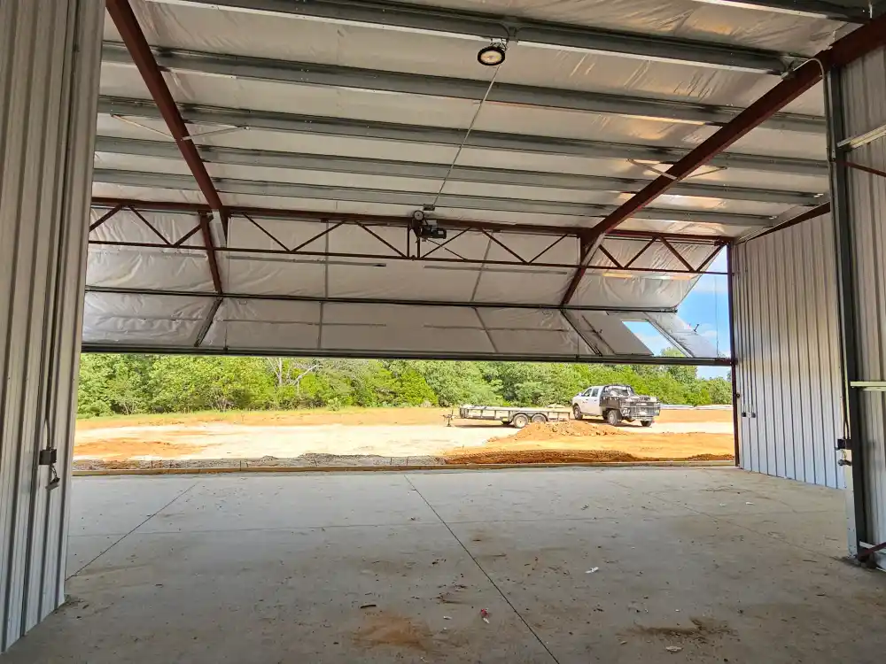 Looking out of a finished metal hangar Pro Phase Electric wired, the bifold door open onto the site