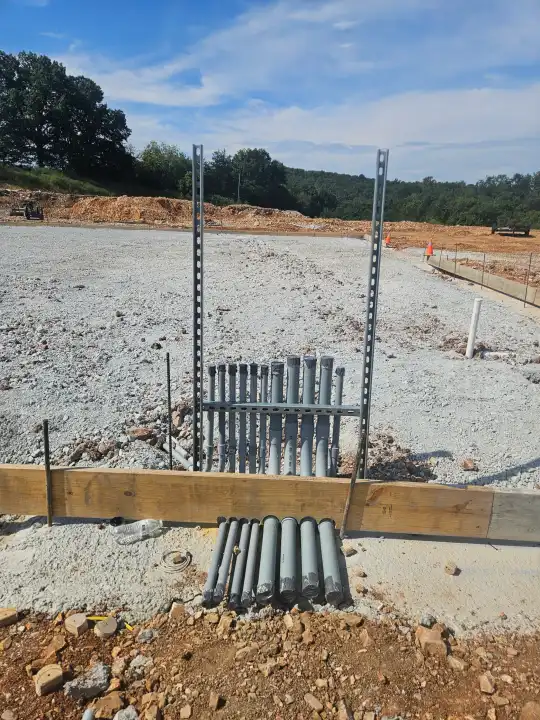 Grey conduit stub-ups and metal strut standing at the edge of a slab form, ahead of the concrete pour