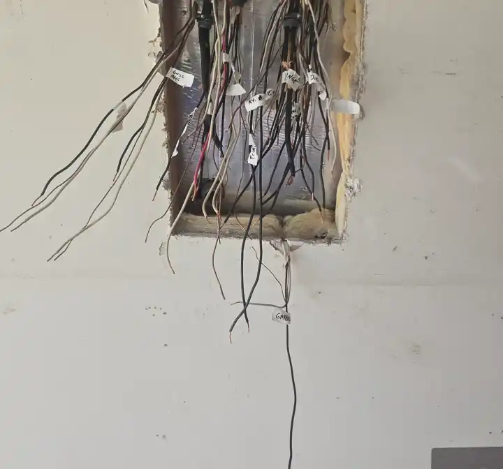 Cables with white tags hanging out of an open rough-in box in an unfinished wall